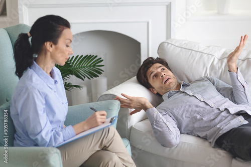 Puzzled guy laying on coach at psychologist cabinet, sharing thoughts