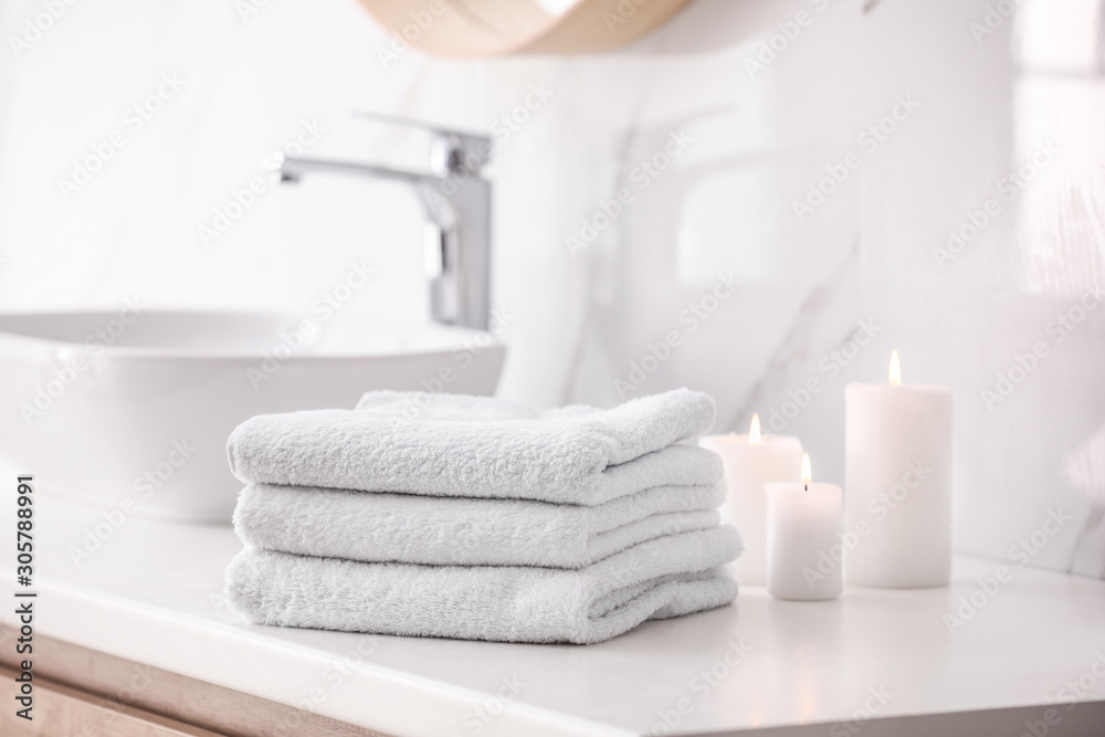 Stack of fresh towels and burning candles on countertop in bathroom - obrazy, fototapety, plakaty 