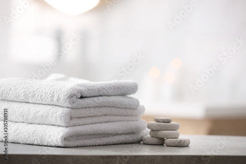 Stack of fresh towels and spa stones on table in bathroom