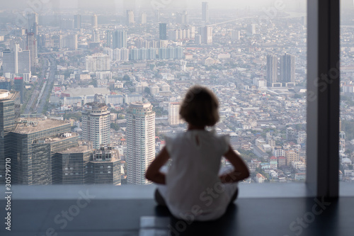 Silhouette of a little girl at the window. Little girl explores the skyscrapers. Concept. Horizontal