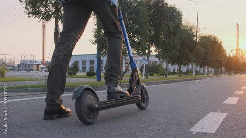 A man starts riding on an electric scooter. Male feet in leather boots stand on an electric scooter at sunset in the Park and starts riding.