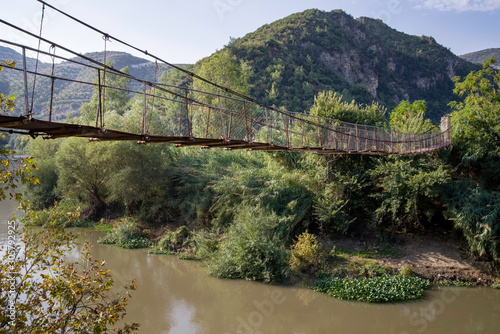 side view of a narrow hung steel bridge over a river at nature