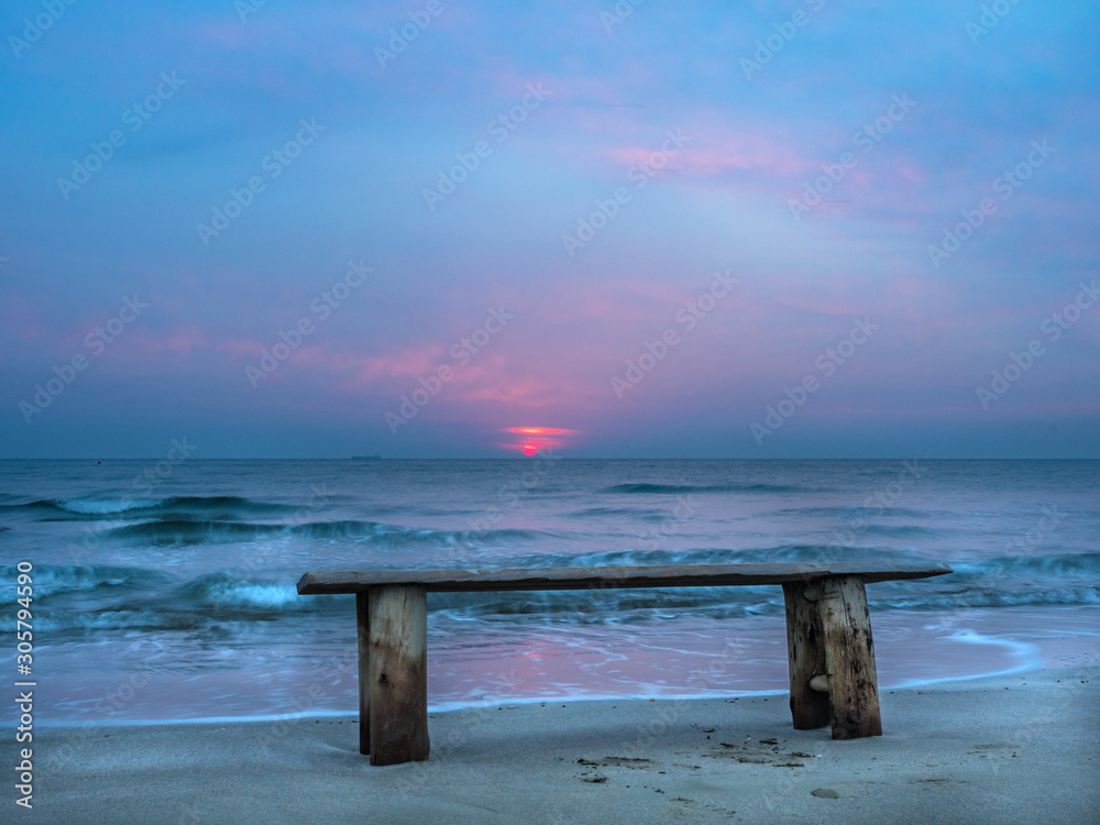 Sunrise on the beach with waves splashing against the shore and wooden bench, Mediterranean, Larnaca, Cyprus