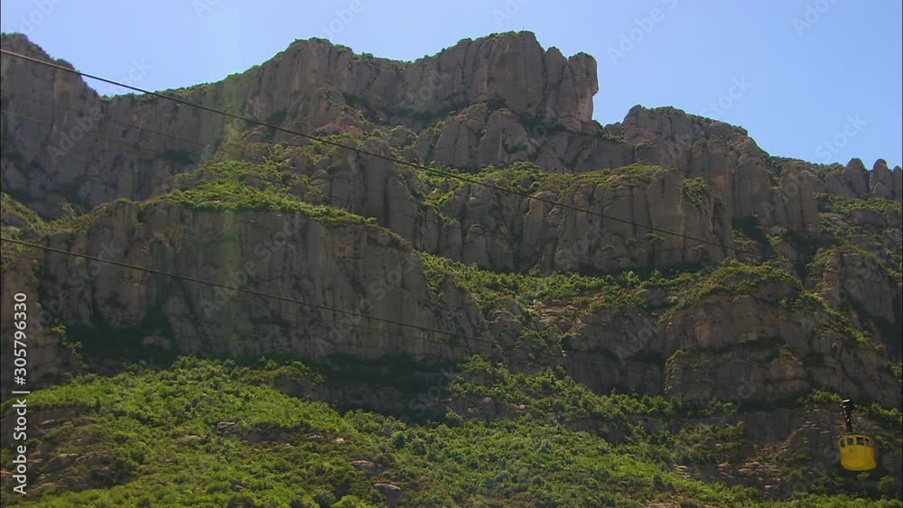 Medium low-angle still shot of Montserrat mountain rocks, and a yellow cable car steadily moving towards the upper station, Montserrat Mountains, Catalonia, Spain Medium low-angle still shot of Montserrat mountain rocks, and a yellow cable car steadily moving towards the upper station, Montserrat Mountains, Catalonia, Spain