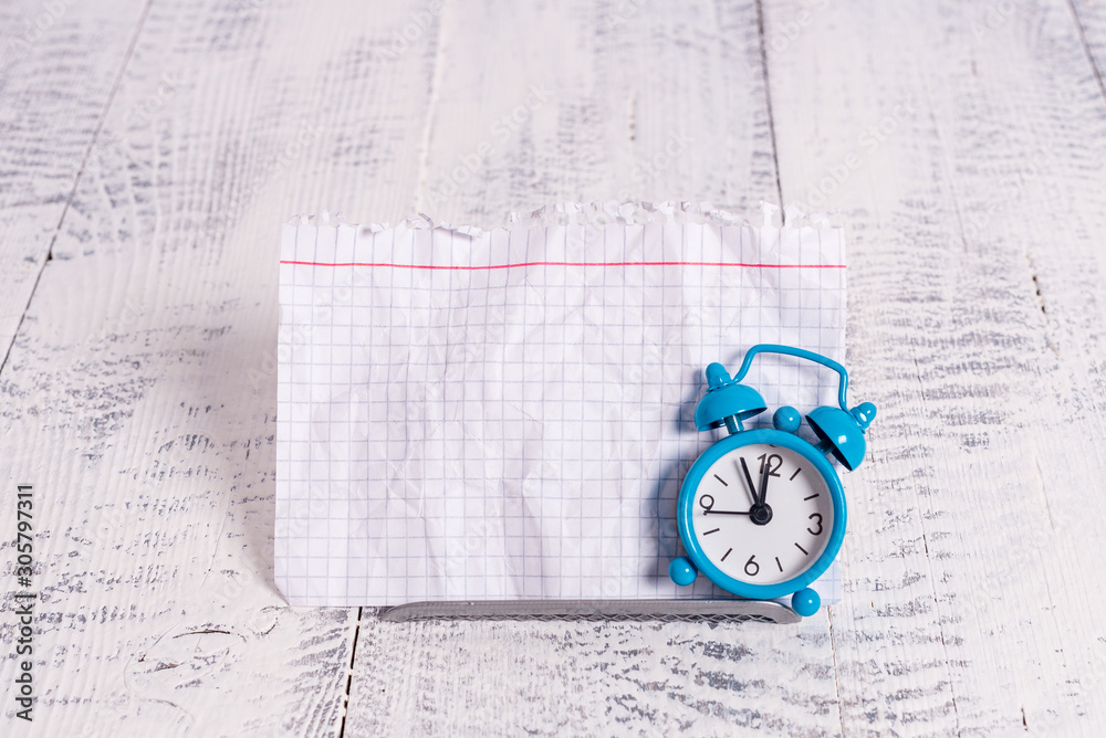 Mini blue alarm clock stand tilted above buffer wire in front of notepaper Mini blue alarm clock stand tilted above buffer wire in front of notepaper