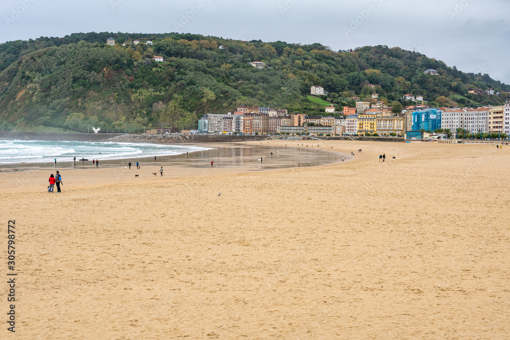 Embankment and city sand beach. San Sebastian, Spain. 26 nov 2019 Rest of people and water sports on the beach in autumn period. Embankment and city sand beach. San Sebastian, Spain. 26 nov 2019 Rest of people and water sports on the beach in autumn period.