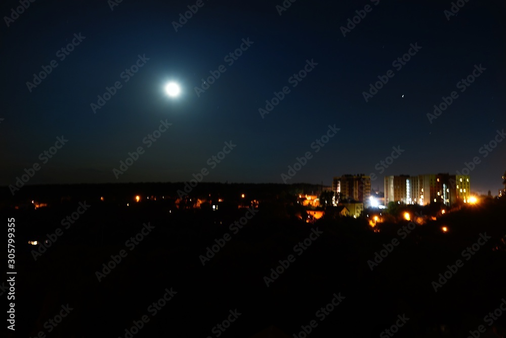 Bright moon in the starry night sky over the city
