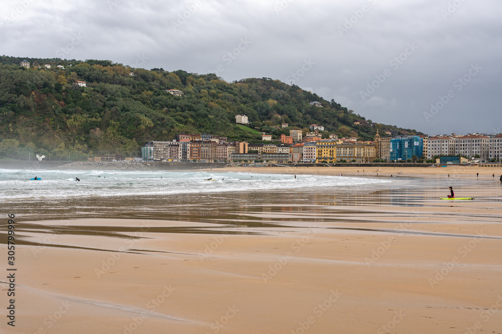 Embankment and city sand beach. San Sebastian, Spain. 26 nov 2019 Rest of people and water sports on the beach in autumn period.