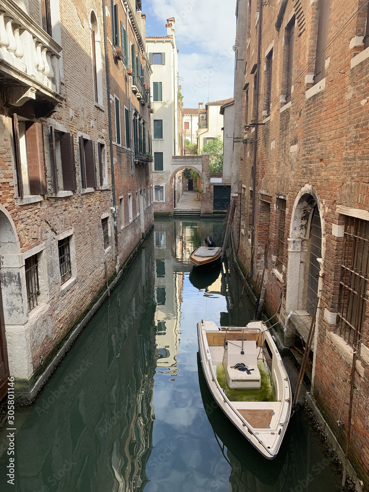 Two old pleasure boats on a leash on the dark dirty water of a narrow canal against the background of dilapidated brick buildings. Sad landscape of the destruction of houses from moisture, flooding .