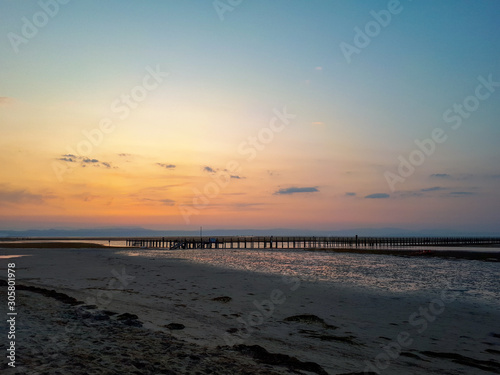 Colorful sunrise sky with pier in the sea during low tide at the beach of Grado