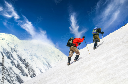 Fotografering Two mountain trekkers on steep snowed hill with dramatic sky background