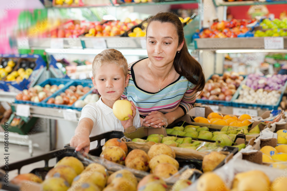 Portrait of happy woman and her little son choosing pears and apples at shop