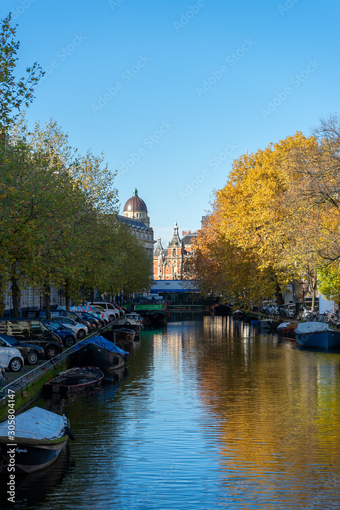 House and boat reflections in the canals of Amsterdam, autumn colors and blue sky