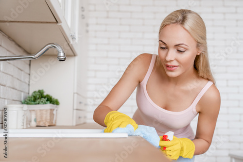 Close up woman cleaning kitchen using cleanser spray and duster