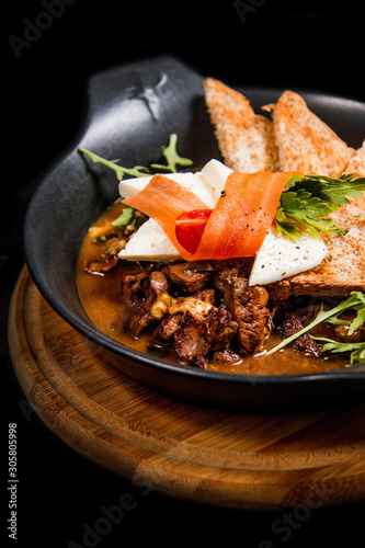 Rustic bowl of cooked beef in sauce, vegetables, decorations and toasted pieces of bread photo