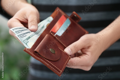 Man putting money into wallet on blurred background, closeup