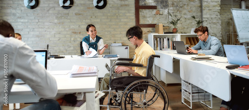 Incredibly doing things rightly. Guy in a wheelchair working in the office photo