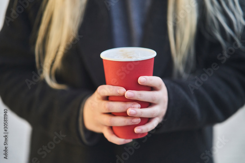 A young girl holds a cup with coffee in her hands. 