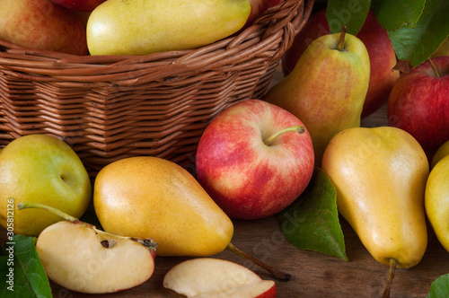 Many ripe tasty apples and pears on a wooden table and in a basket with leaves. Harvest fruit.