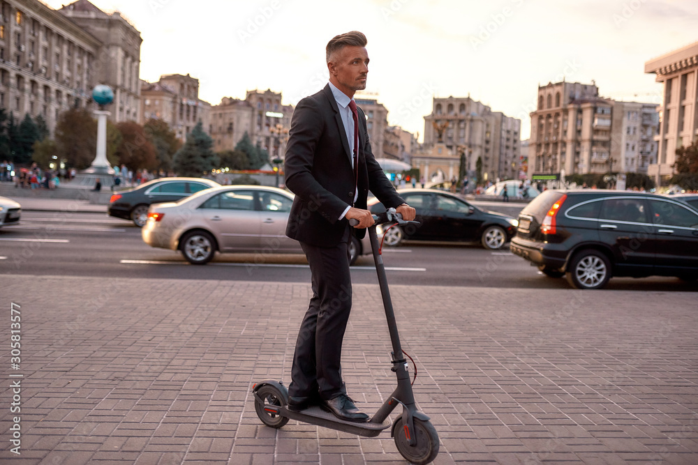Easy and comfortable. Businessman on daily commute riding scooter along the street
