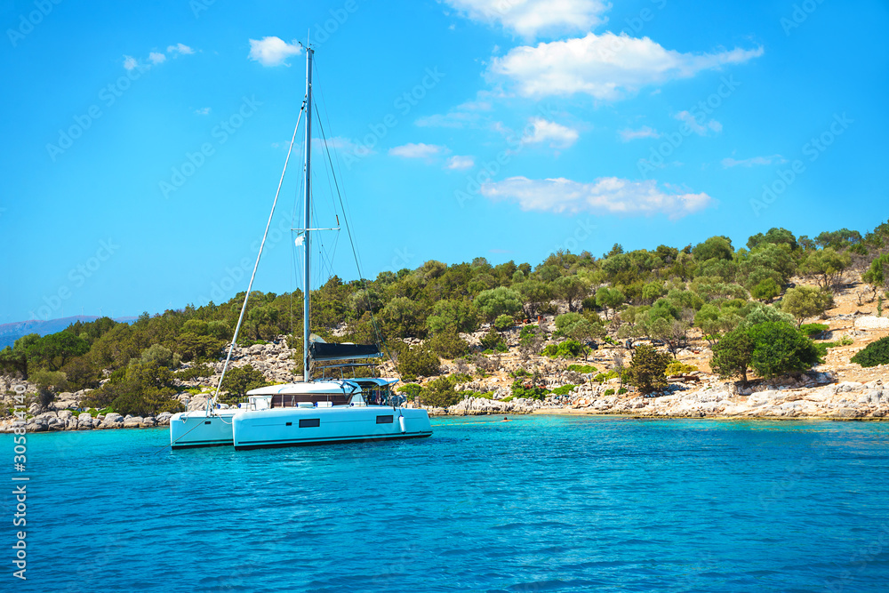 Sailing yacht catamaran boat with white sails on turquoise waters of sea.