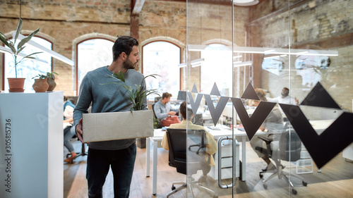 Saying good bye. Handsome man in casual wear holding box with personal things and leaving modern office photo