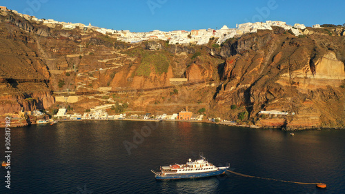 Aerial drone photo of luxury yacht docked near old port of Santorini island in deep blue sea just below village of Fira at sunset, Cyclades, Greece