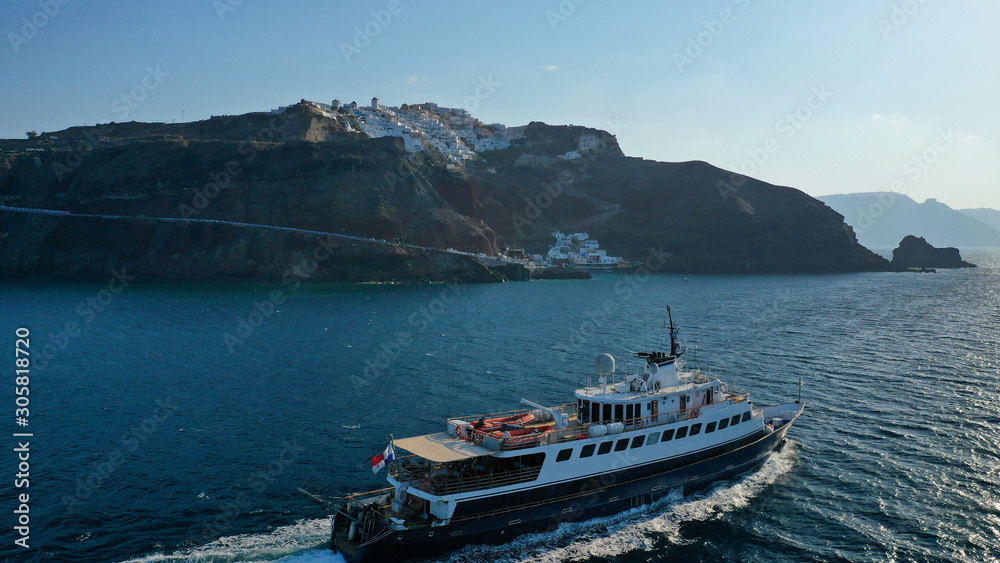 Aerial drone photo of luxury yacht cruising near iconic village of Oia, Santorini island, Cyclades, Greece