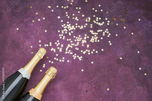 Two Champagne bottles with golden confetti on purple background. Flat lay of Christmas celebration concept. Copy space.