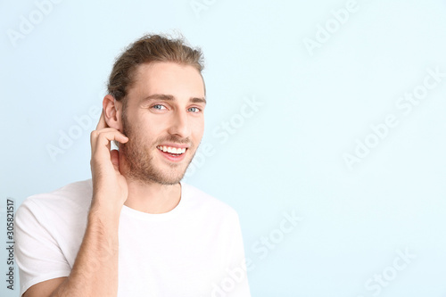 Young man with hearing aid on color background