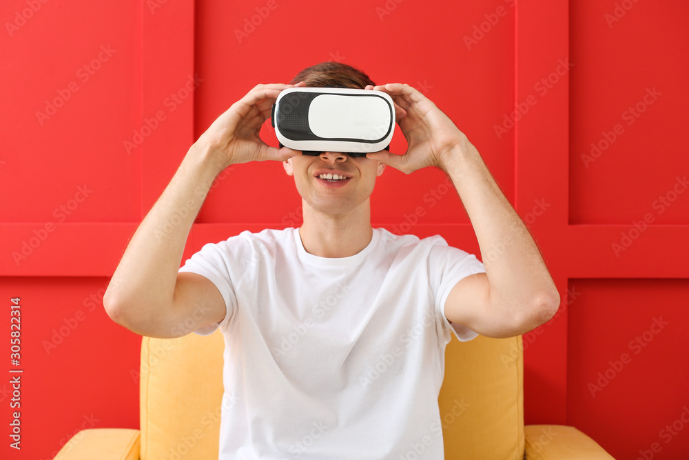 Young man with virtual reality glasses sitting in armchair on color background Young man with virtual reality glasses sitting in armchair on color background