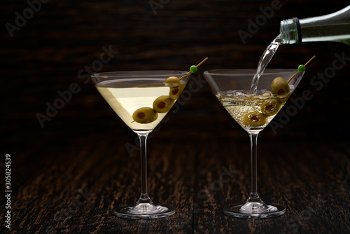 Pouring martini from the bottle into the glass against  wooden background.