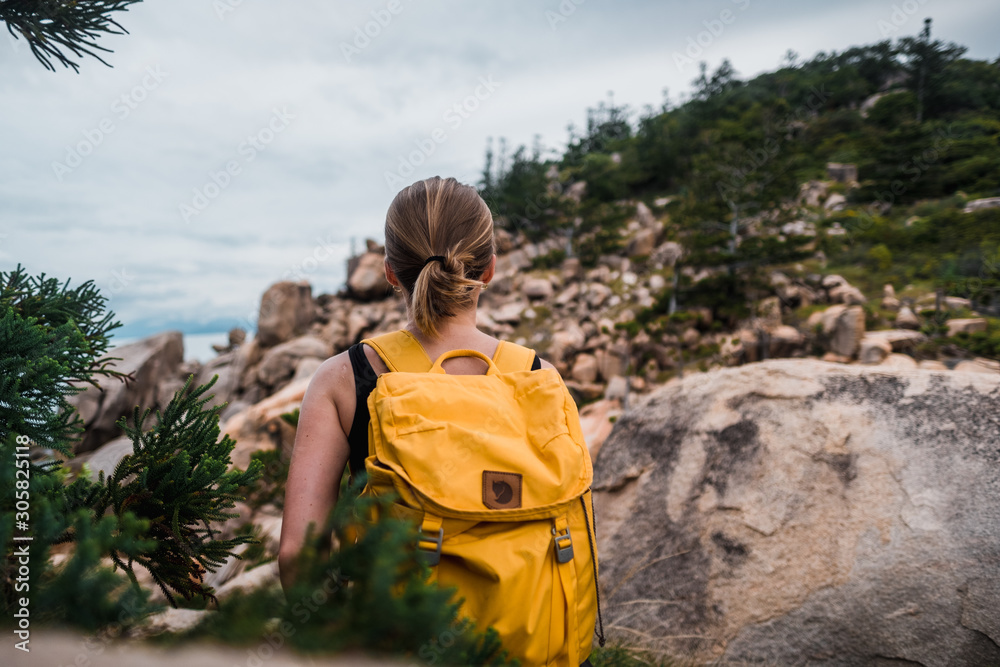 Young attractive girl wearing backpack and hiking in the rocky coastline in Australia