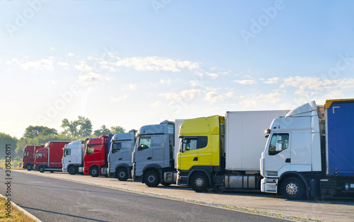 Various types of trucks in the parking lot next to the motorway.