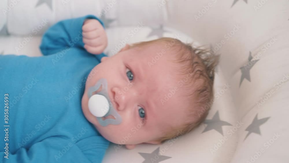 sad little newborn baby in blue bodysuit with pacifier lies in comfortable sleeping cocoon at home closeup sad little newborn baby in blue bodysuit with pacifier lies in comfortable sleeping cocoon at home closeup