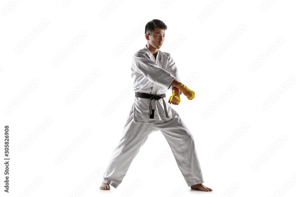 Naklejka premium Confident korean man in kimono practicing hand-to-hand combat, martial arts. Young male fighter with black belt training isolated on white studio background. Concept of healthy lifestyle, sport.