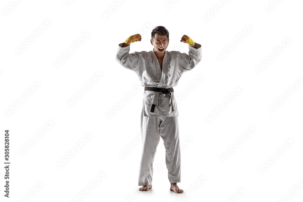 Obraz premium Confident korean man in kimono practicing hand-to-hand combat, martial arts. Young male fighter with black belt celebrates win isolated on white studio background. Concept of healthy lifestyle, sport.