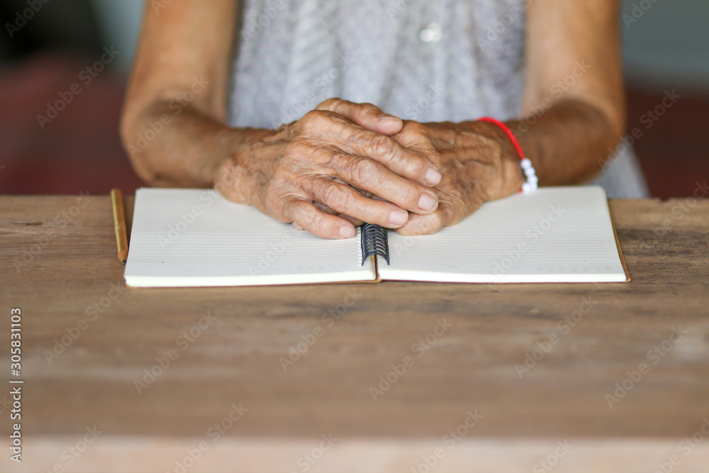 Old woman hands on notebook on wooden table Old woman hands on notebook on wooden table