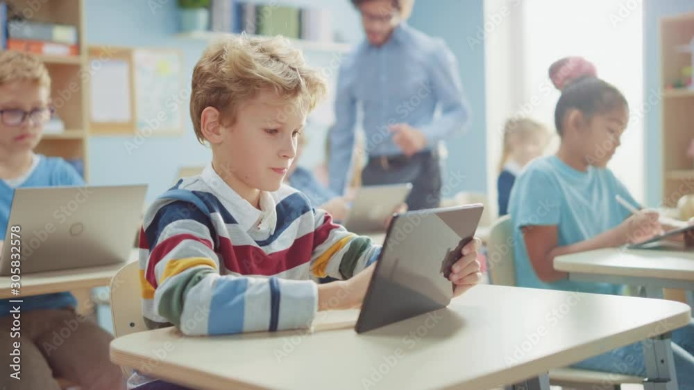Elementary School Computer Science Class: Cute  Boy Uses Digital Tablet Computer, His Classmates work with Laptops too. Children Getting Modern Education in STEM, Playing and Learning
