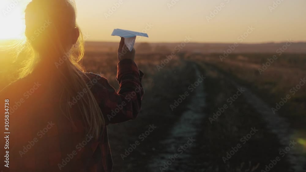Happy little girl playing with a paper airplane outdoors during sunset ...