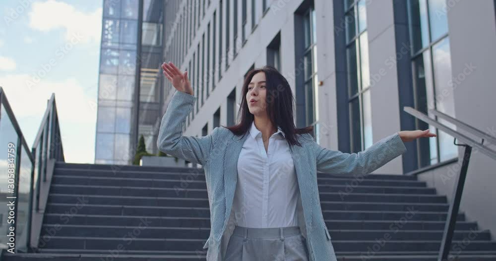 Caucasian young businesswoman dancing cheerfully and moving funny while being outdoor at the big modern office center after successful meeting and sighing a contract. Caucasian young businesswoman dancing cheerfully and moving funny while being outdoor at the big modern office center after successful meeting and sighing a contract.