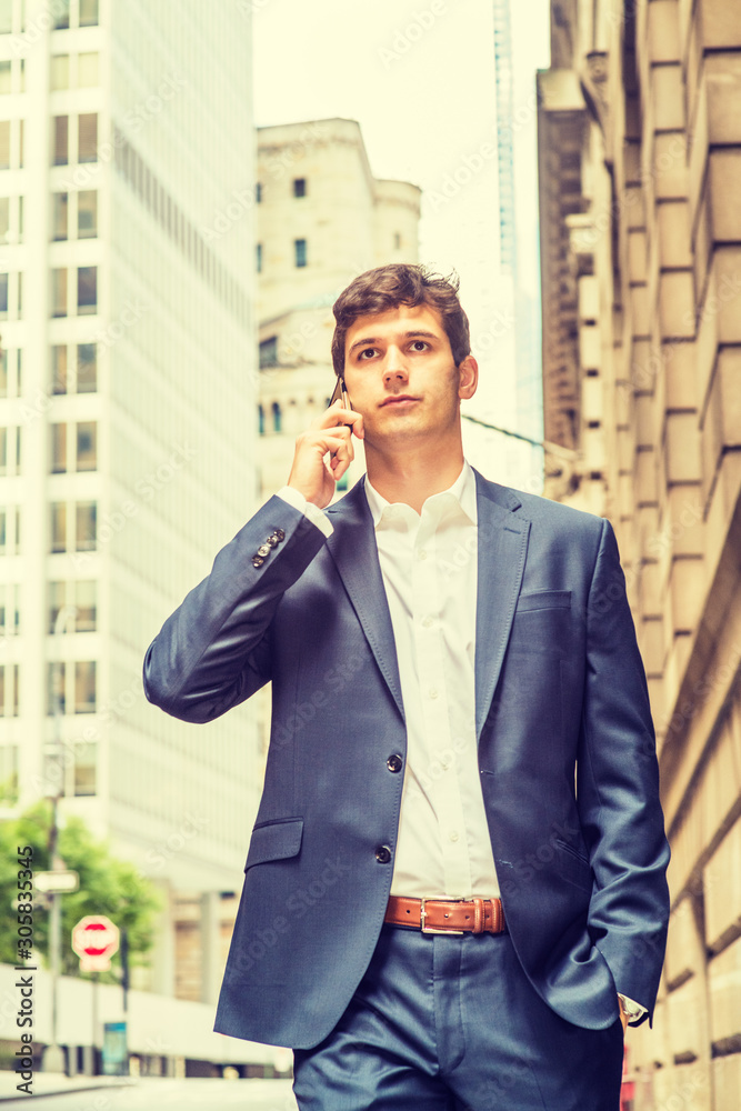 Modern daily life. Young handsome man traveling in New York City, wearing blue suit, white shirt, hand in pocket, walking on street with high buildings, talking on cell phone, looking, thinking.. Modern daily life. Young handsome man traveling in New York City, wearing blue suit, white shirt, hand in pocket, walking on street with high buildings, talking on cell phone, looking, thinking..