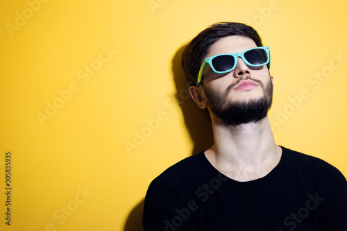 Portrait of young hipster, wearing cyan sunglasses, isolated on yellow background.