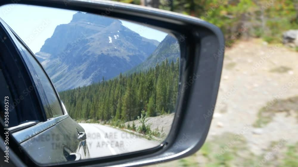 View of side mirror of the moving car while on the local road moving along the local way through the Banff National park in Alberta in Canada View of side mirror of the moving car while on the local road moving along the local way through the Banff National park in Alberta in Canada