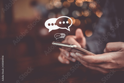 Women hand using smartphone mobile typing, chatting conversation in chat box icons pop up. Social media maketing technology concept.Vintage soft color tone background. photo