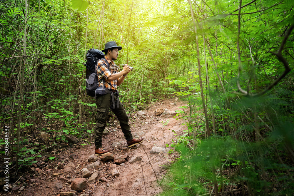 man traveler holding camera with backpack standing in the forest