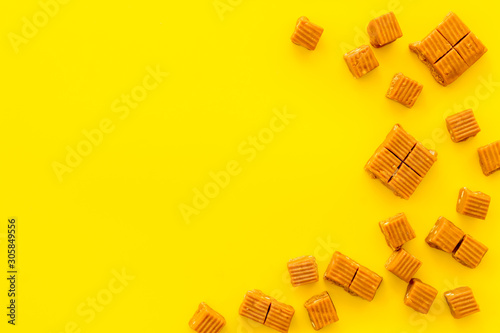 Caramel candies cubes on yellow background top view frame copy space