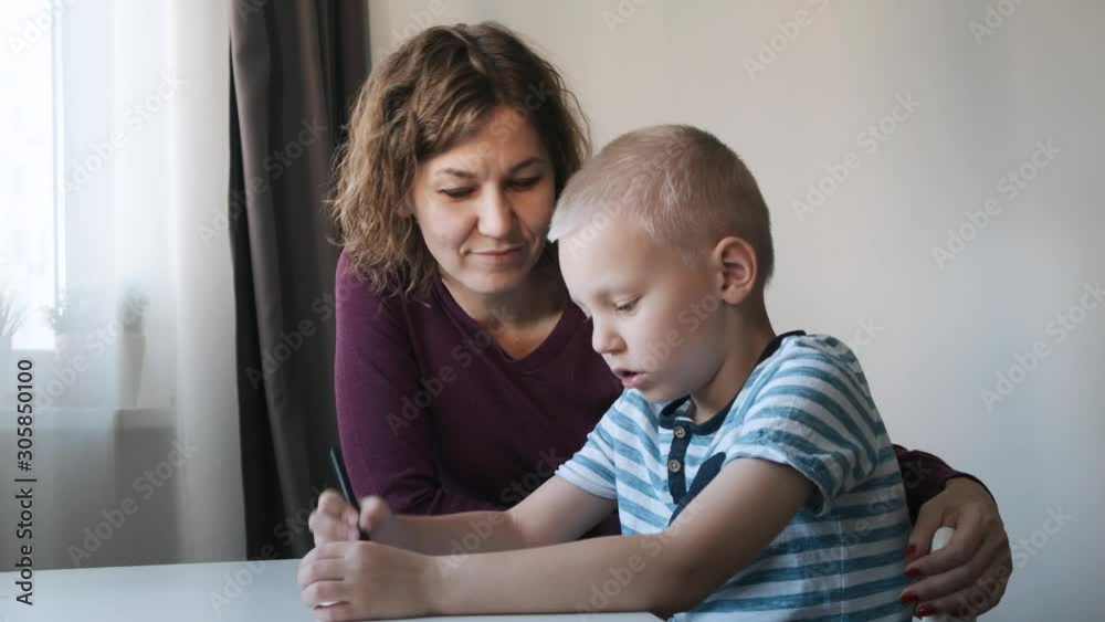 Child boy sitting at the table at home and drawing together with their mom. Family concept Child boy sitting at the table at home and drawing together with their mom. Family concept