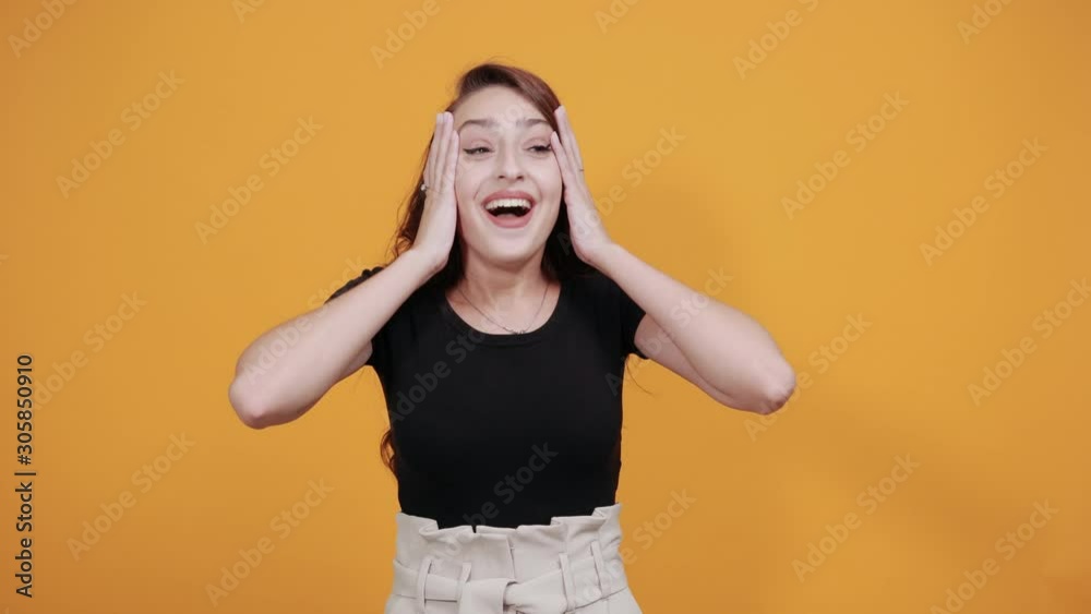 Shocked young woman in black shirt covered mouthh with hands, keeping hands on chest isolated on orange background in studio. People sincere emotions, health concept. Shocked young woman in black shirt covered mouthh with hands, keeping hands on chest isolated on orange background in studio. People sincere emotions, health concept.