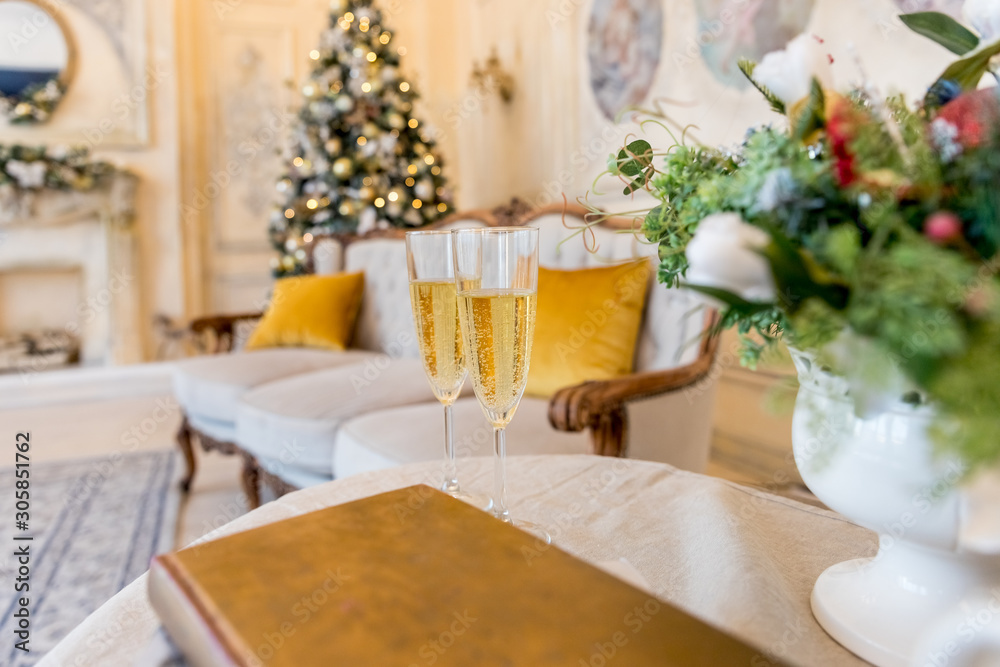 New Year and Christmas Celebration. Two Champagne Glasses over Golden Blinking christmas tree, Holiday Background.invitation.Romantic champagne flutes in front of a christmas tree.Holiday Celebrating